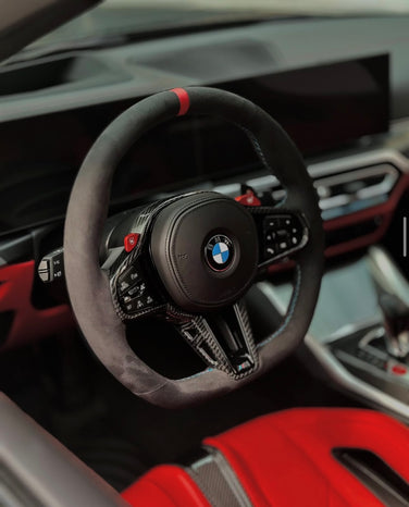 Close-up of a BMW custom steering wheel with red accents in a car interior.