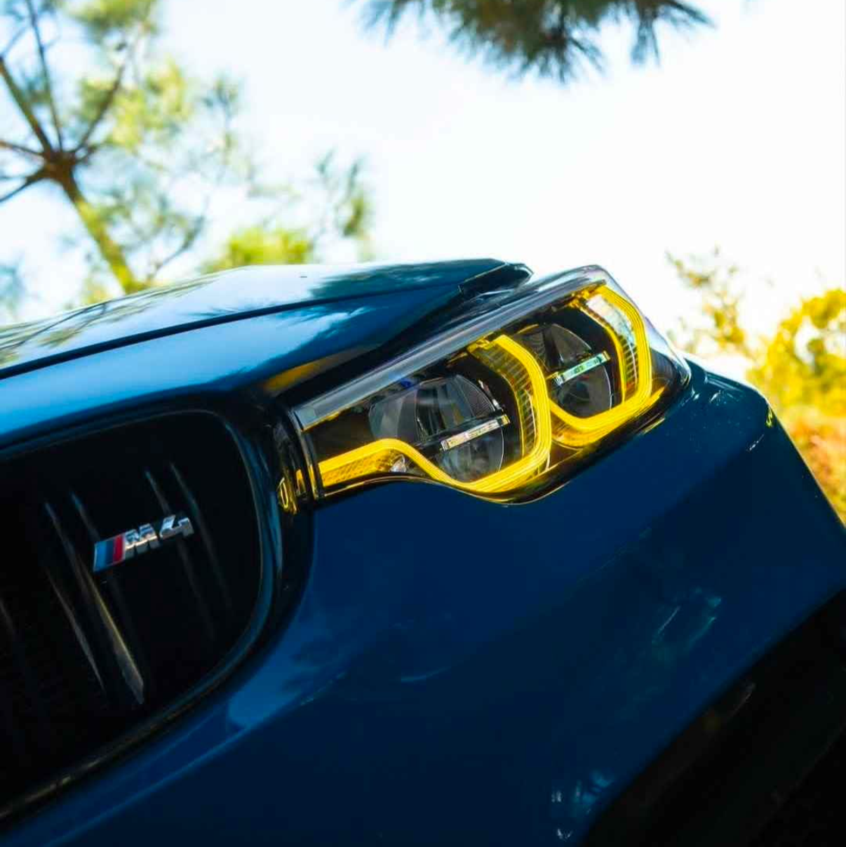Close-up of a bmw m4 headlight with yellow accents against a blurred natural background